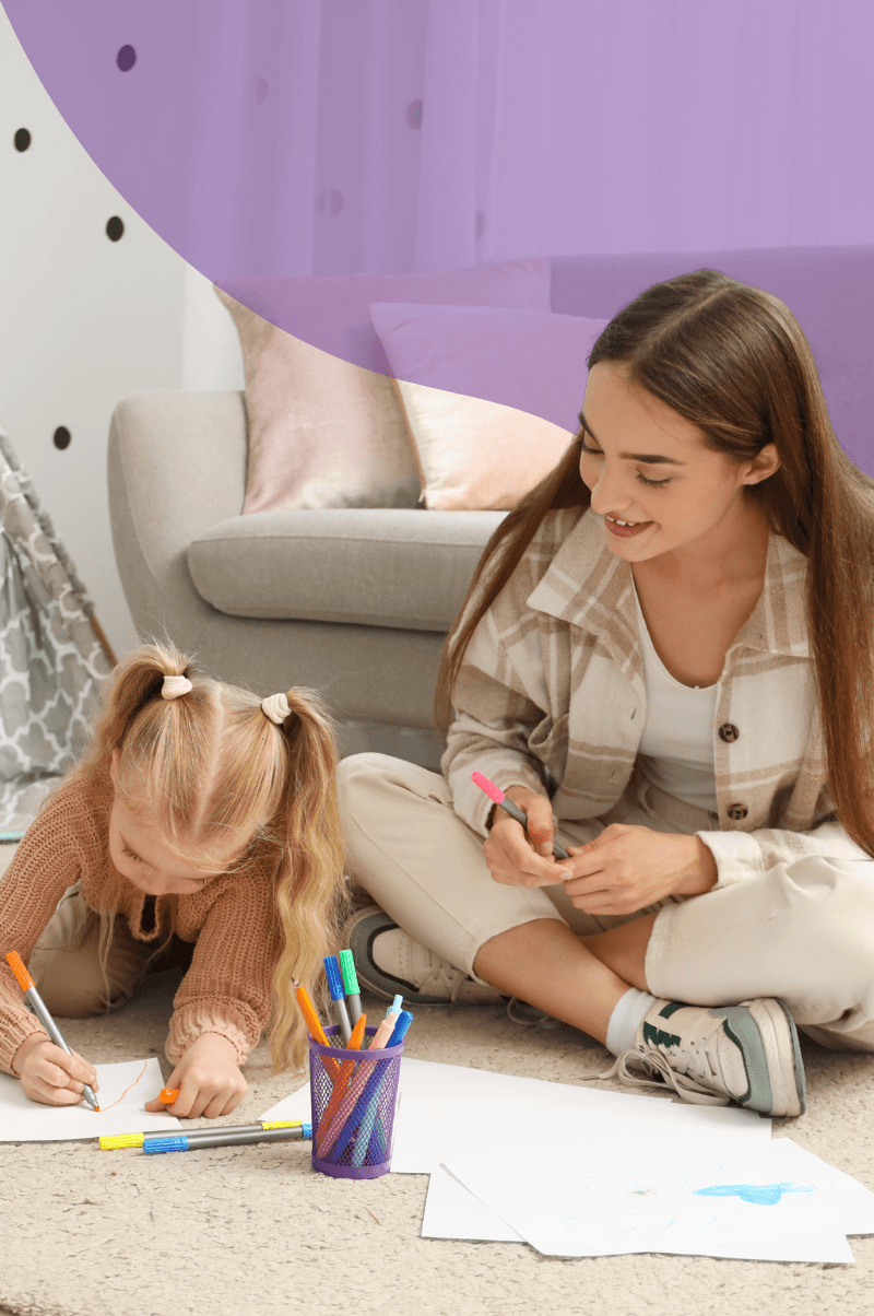 Young au pair doing arts and crafts with a child on the floor at home in South Africa